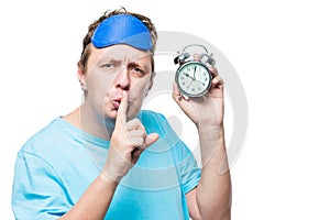 Man with an alarm clock showing a gesture quietly in a mask for