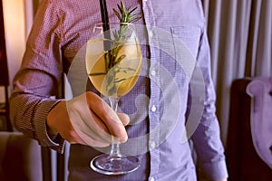 Man with alcohol cocktail with sparkling wine, ice and liquor in wineglass, puts it on the table. Hands close-up.