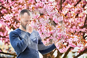 Man allergic suffering from seasonal allergy at spring in blossoming garden.