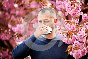 Man allergic suffering from seasonal allergy at spring, sneezing and blowing nose with handkerchief.