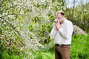 Man allergic suffering from seasonal allergy at spring, sneezing and blowing nose with handkerchief.