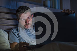 Man alone in bed playing cybersex using laptop computer watching sex movie late at night with lascivious pervert face