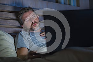 Man alone in bed playing cybersex using laptop computer watching sex movie late at night with lascivious pervert face