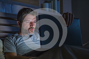 Man alone in bed playing cybersex using laptop computer watching sex movie late at night with lascivious pervert face