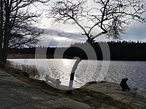 Man alone on rock taking photos in front of a lake in the sun