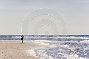 Man alone walking along the dutch coastline on a sunny day with the sunlight reflecting in the water