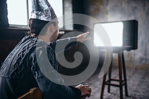 Man in aluminum foil helmet reaches out to the TV