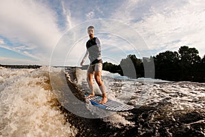 man with an amputated hand is surfing on surfboard trails behind boat. Wakesurfing