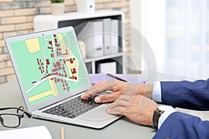 Man analyzing cadastral map on laptop at table, closeup