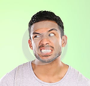 Man, angry face and disgust with awkward humor, comedy or nasty look on a green studio background. Frustrated male photo