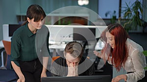 Man with angry facial expression sitting at computer in office listening dissatisfied women talking gesturing in slow