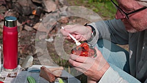 A man with appetite eats canned fish in tomato sauce with a fork. Outdoor picnic