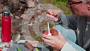 A man with appetite eats canned fish in tomato sauce with a fork. Outdoor picnic