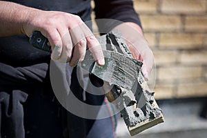 Man applies glue with a spatula on a decorative facing brick, view close up. Construction work, process of wall cladding