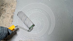 A man applies gray paint with a roller to a concrete floor. Roller with gray paint, close-up.