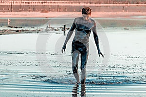 Man applying black healing clay. Mud spa on the shore of salt lake. Swimming in the nutrient-rich mud of the mud lake near the Sea