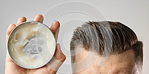 Man applying a clay, pomade, wax, gel or mousse from round metal box for styling his hair after barbershop hair cut