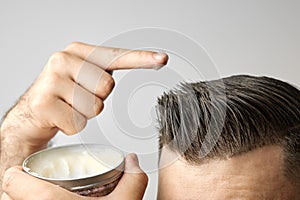 Man applying a clay, pomade, wax, gel or mousse from round metal box for styling his hair after barbershop hair cut