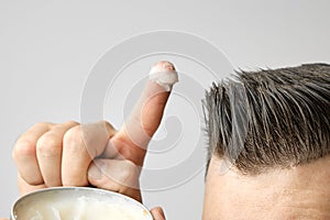 Man applying a clay, pomade, wax, gel or mousse from round metal box for styling his hair after barbershop hair cut