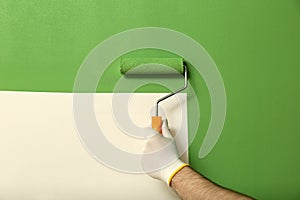 Man applying green paint with roller brush on white wall, closeup
