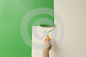 Man applying green paint with roller brush on white wall, closeup