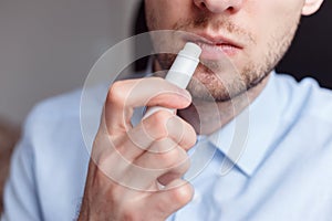 Man applying hygienic lipstick on lips to revive chapped lips and avoid dry, closeup