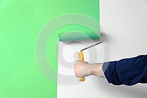 Man applying light blue paint with roller brush on white wall, closeup