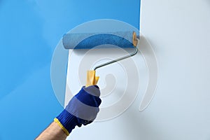 Man applying light blue paint with roller brush on white wall, closeup