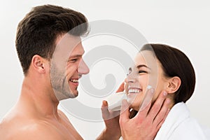 Man applying moisturizer on woman's cheek