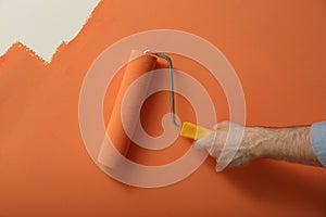 Man applying orange paint with roller brush on white wall, closeup