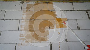 Man applying orange paint with roller brush on white wall, closeup. Orange paint is applied to the wall.