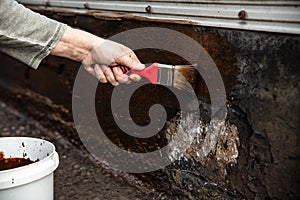 man applying primer with a brush to a damaged bitumen coating photo