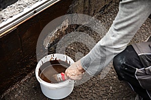 man applying primer with a brush to a damaged bitumen coating photo