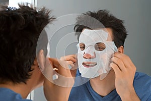 Man is applying a rejuvenating cosmetic textile mask on face.