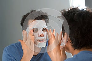 Man is applying a rejuvenating cosmetic textile mask on face.