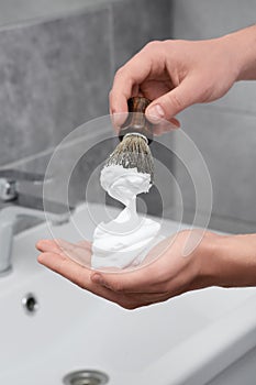 Man applying shaving foam onto brush in bathroom, closeup