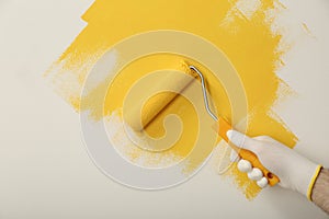 Man applying yellow paint with roller brush on white wall, closeup