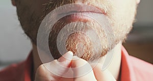 Man approaches the camera and strokes his beard. Blurred background, close-up. The concept of thoughtfulness, reflection