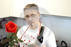 A man in an apron cooks in the kitchen and meets his girlfriend, offering a rose and wine.