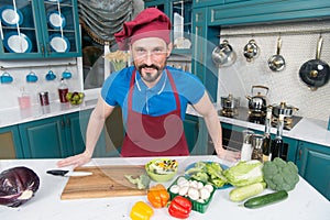 A Man in apron in the kitchen doing salad for vegans. Handsome man cooking at home preparing salad in kitchen. Handsome happy male
