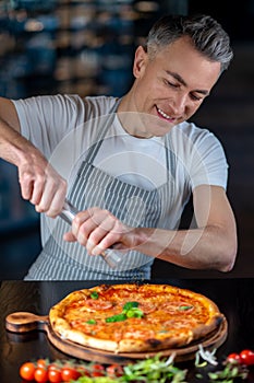 A man in apron making vegetarian pizza with cherry tomatos