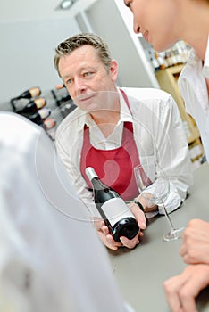 Man in apron showing bottle wine to couple