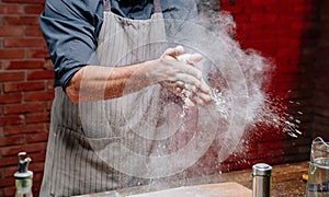 man in an apron take flour and clap their hands. scatter the flour