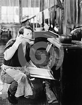 Man with an apron tasting food in front of an oven in a kitchen