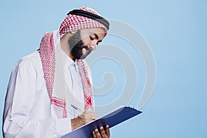 Man in arab thobe writing in clipboard