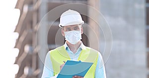 Man architect in protective mask inspecting building, checking real estate plan at construction site