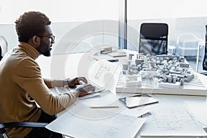 Man architect working with software on laptop using technical drafts drawings at office workplace