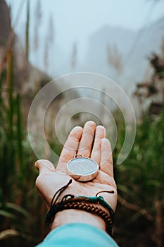 Man arm with compass on the palm stretched out to determine position in mountains on cloudy day