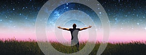 Man with arms wide open standing on the grass field against the night starry sky. Elements of this image furnished by