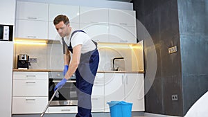 Man as a professional cleaner in blue uniform washing floor with mopping stick and bucket in the kitchen of the